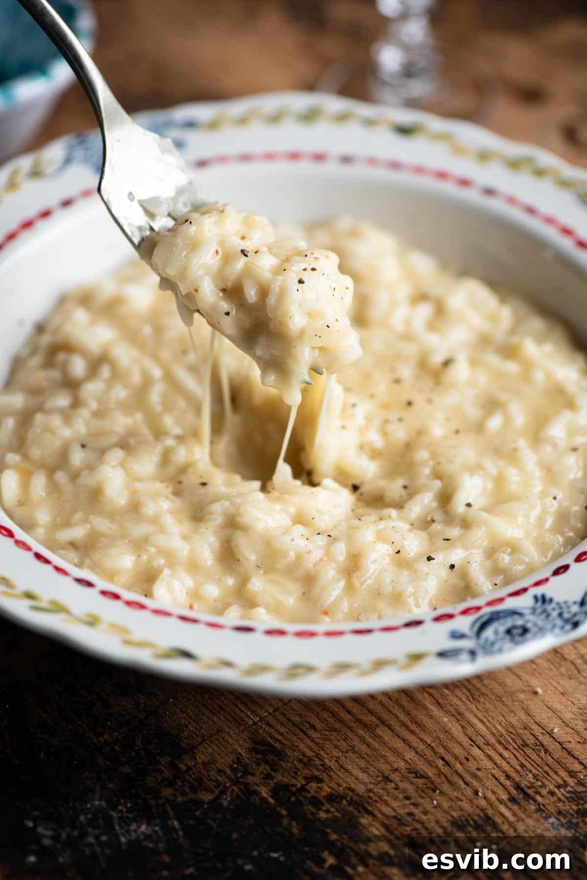 Creamy Fontina Risotto 7 A close up of a fork picking up cheesy risotto from a bowl, highlighting its creamy texture.