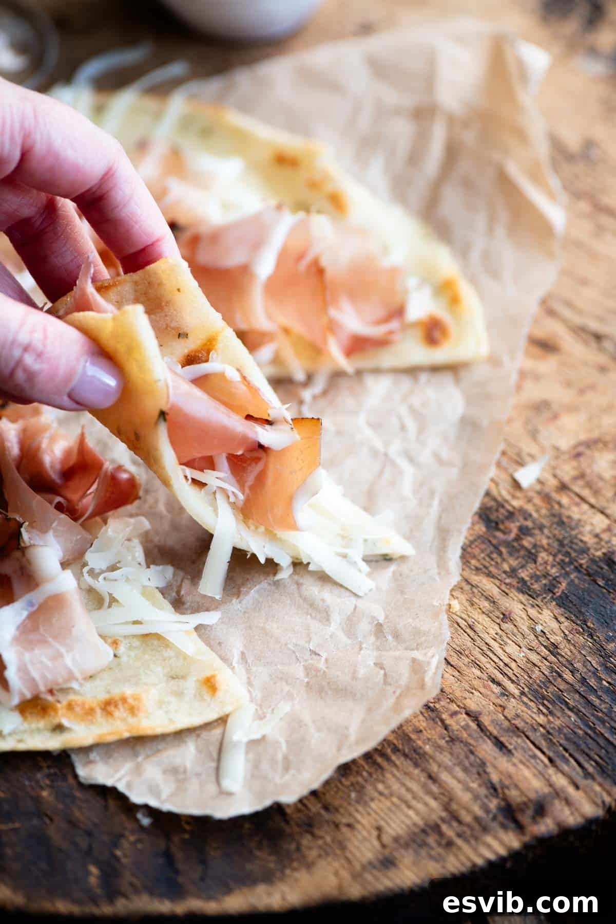 Brustengo: Umbria's Rustic Flatbread 6 A hand picking up a slice of Italian flatbread topped with cured meat and cheese.