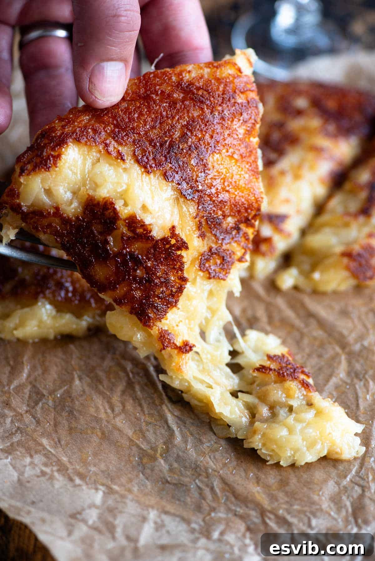 Golden Cheesy Potato Onion Cake 7 A hand picking up a slice of fried cheese and potato (frico) from a wooden board, showing the delicious golden crust.