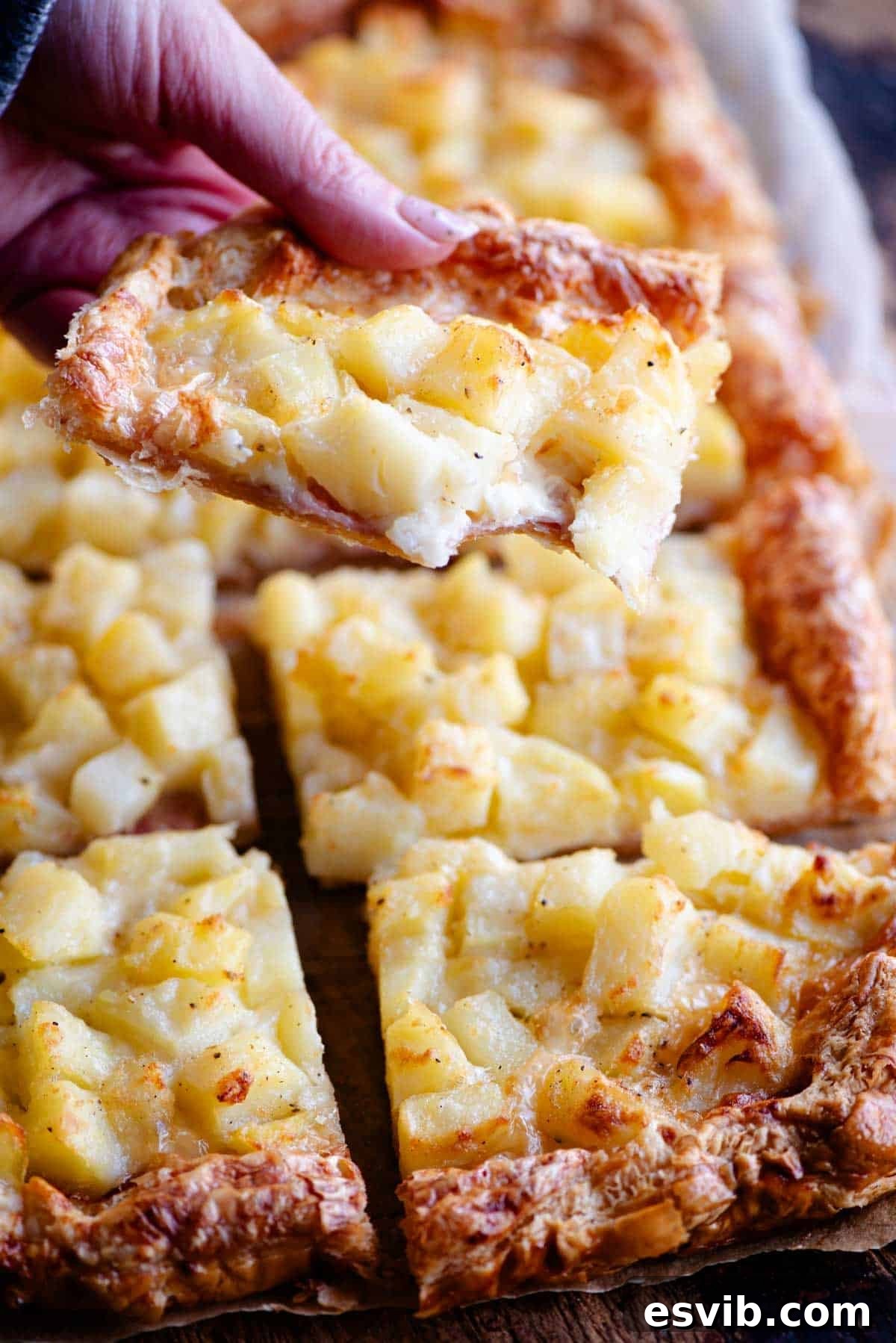 Flaky Potato & Cheese Tart 6 A close up of a hand holding a slice of puff pastry and potato tart.