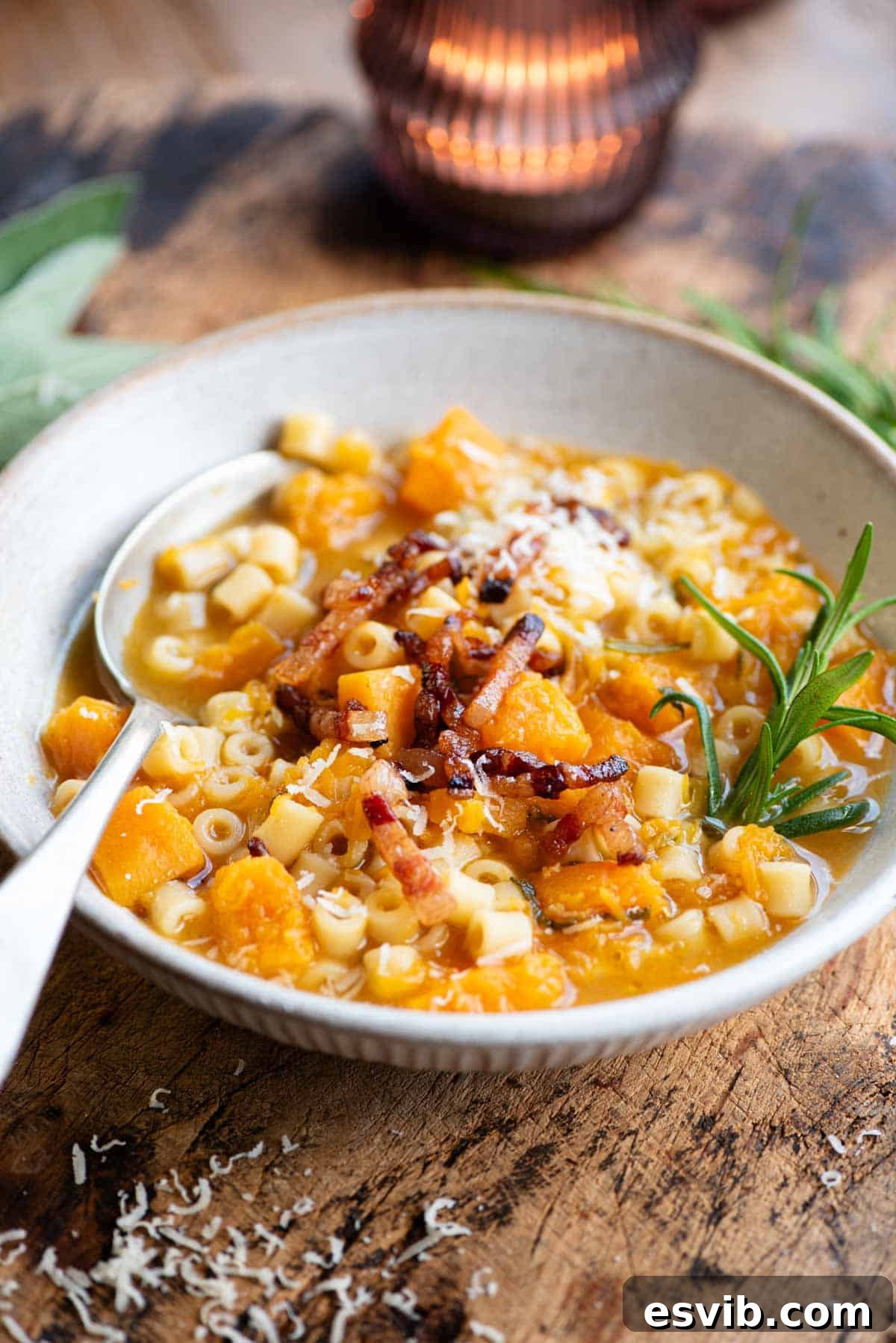 Velvety Butternut Squash Pasta Soup, Crispy Pancetta Finish 2 A butternut squash and pasta soup topped with pancetta and a sprig of rosemary. The bowl is on a wooden table.