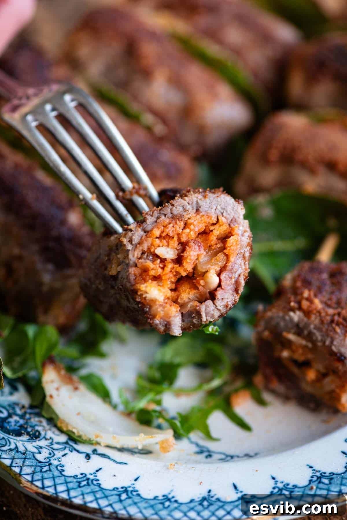 A close-up shot of one Sicilian stuffed beef roll, cut in half to reveal its rich, flavorful filling on a fork.