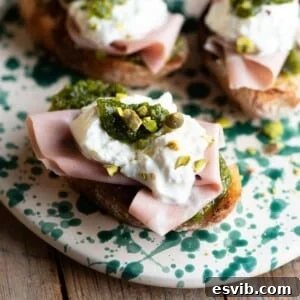 A close up cropped image of mortadella crostini with burrata and pistachios.