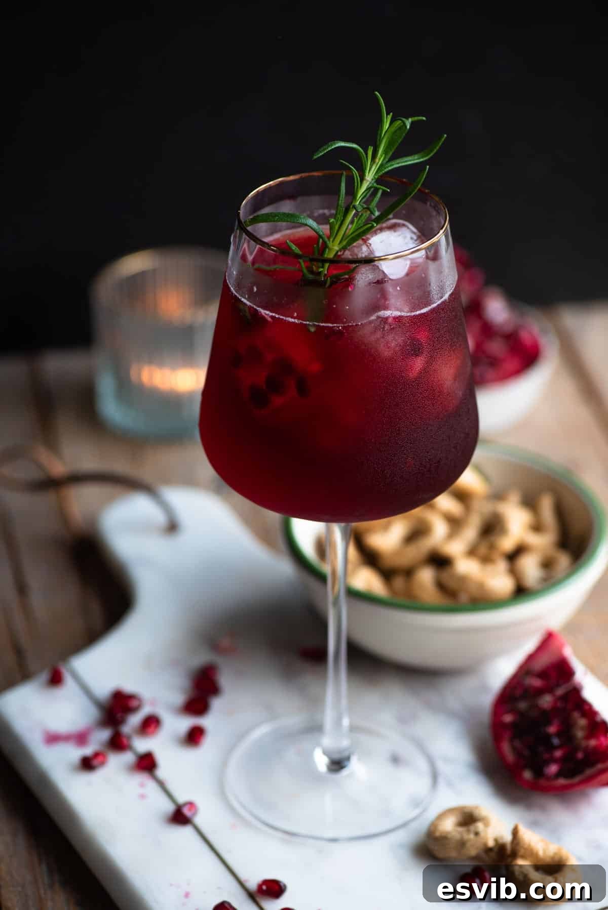Crimson Sparkler 2 A vibrant Pomegranate Spritz served in a tall, gold-rimmed wine glass, beautifully garnished with a sprig of fresh rosemary and glistening pomegranate arils. The drink's rich red hue promises a refreshing and festive experience.