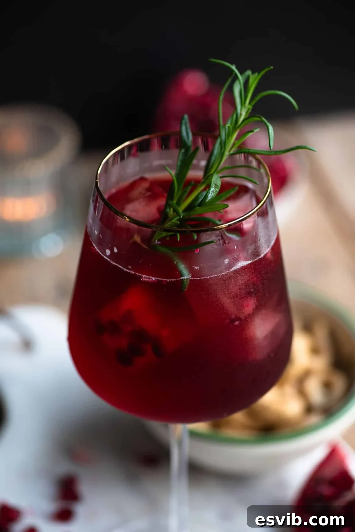 Crimson Sparkler 4 A vibrant close-up of a Pomegranate Spritz in a tall wine glass, beautifully garnished with a sprig of fresh rosemary and a few floating pomegranate arils, highlighting its rich, inviting color and effervescent top.