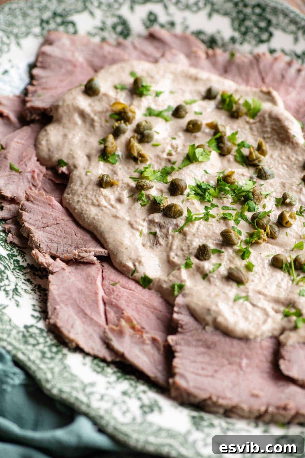 A close-up shot of individual servings of Vitello Tonnato, highlighting the tender veal slices and the luscious, creamy tuna sauce with caper and parsley garnish.