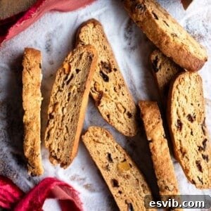 A cropped square image of cantucci biscotti on a wooden surface dusted in sugar.