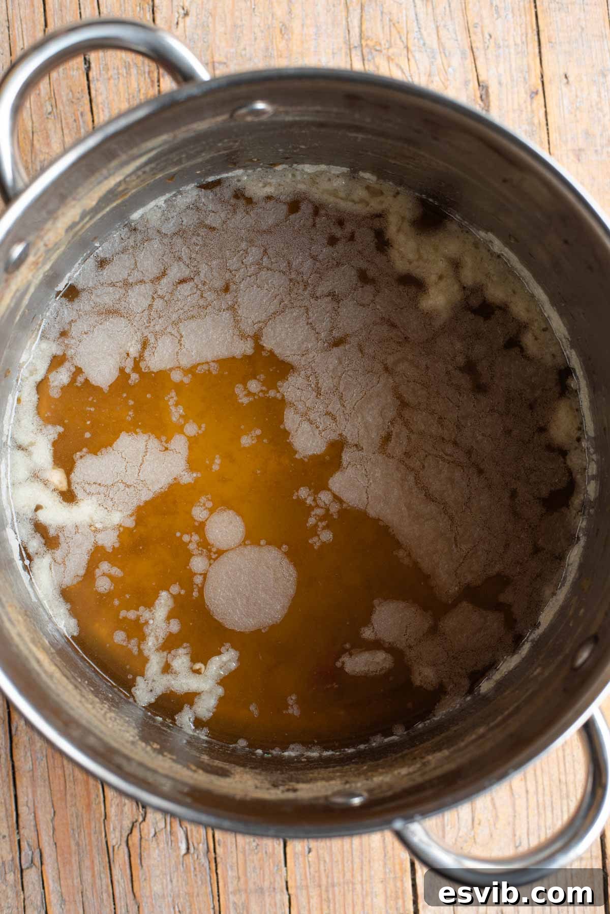 A detailed photo showing a clear, solidified layer of fat resting on top of cooled Italian meat broth in a large, transparent bowl, ready for skimming.
