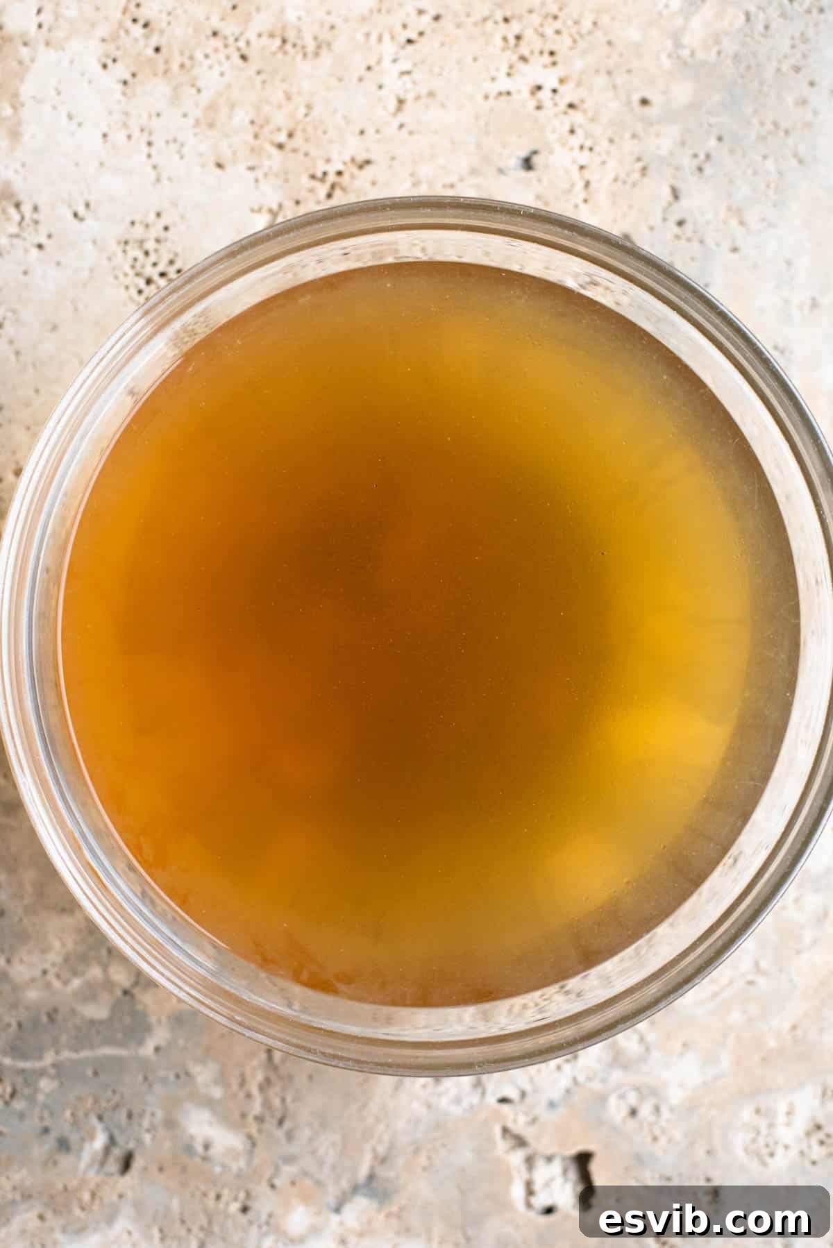 An overhead shot of clear, golden Italian broth 'brodo di carne' served elegantly in a beautiful glass bowl, ready for culinary use or immediate enjoyment.