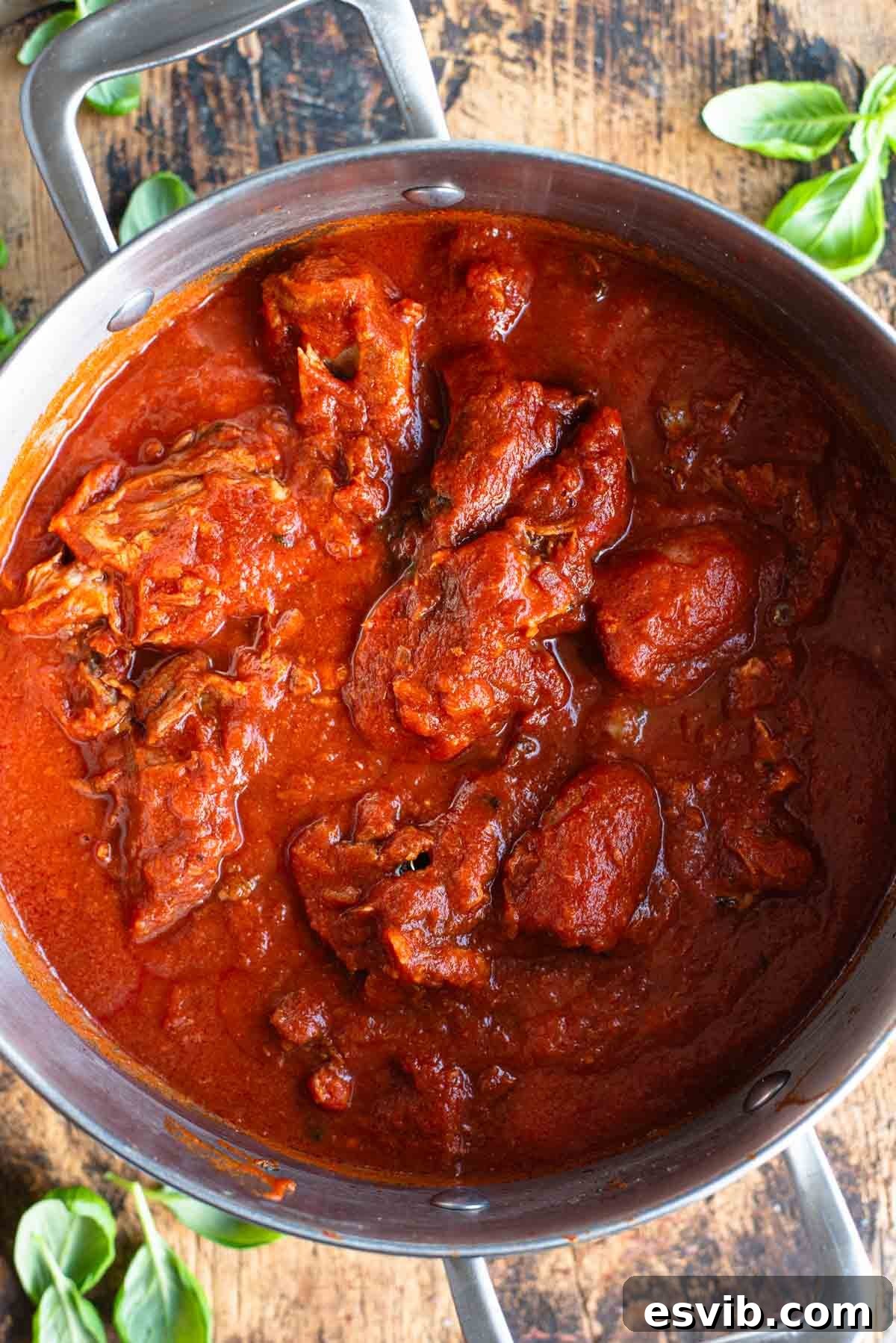 An overhead shot of Sugo Napoletano (Neapolitan ragu) in a large pot sitting on a wooden surface.