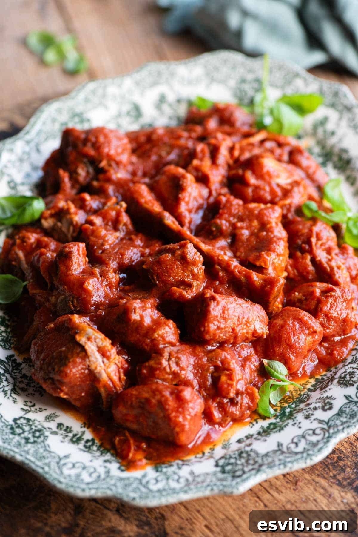 A side shot of lots of cooked meat in tomato sauce on a large serving plate.