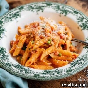 A cropped square image of a bowl of creamy tomato penne pasta on a wooden table.