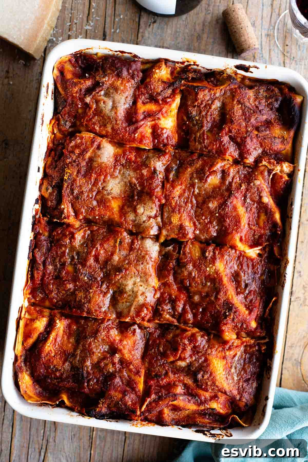 An overhead shot of a Neapolitan lasagna sitting on a wooden table with a bottle of wine at the side, showcasing its rich, golden-brown crust and layered texture.