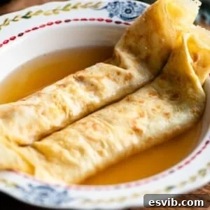 A square cropped image of two crepes in a bowl with broth.