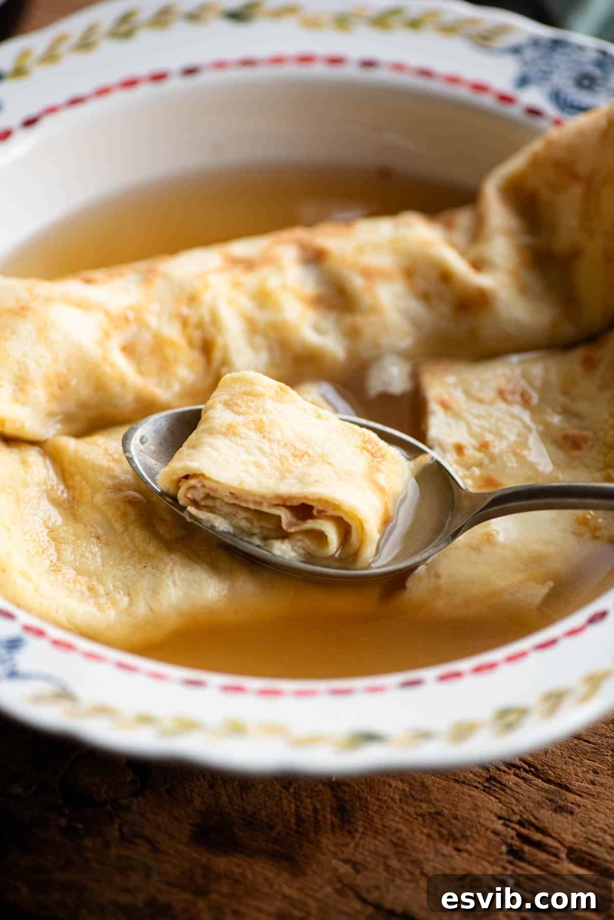 A close up of a spoon in a bowl of broth picking up a spoonful of crepe.