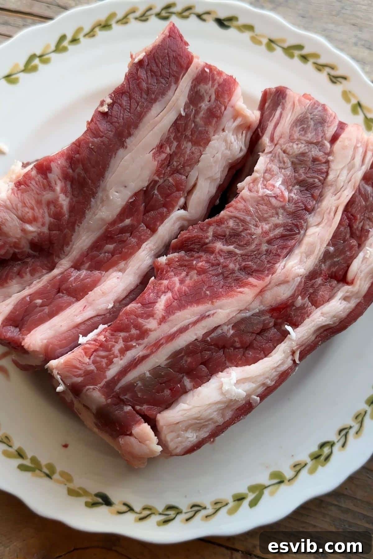 A close-up view of two substantial beef short ribs on a plate with the lifter muscle attached, a common cut in UK butchery, showcasing marbling.