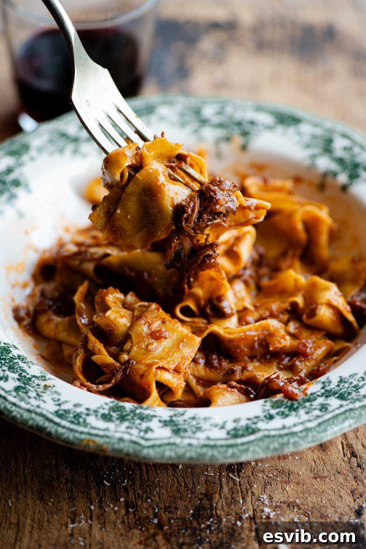 A side shot featuring a fork lifting a perfect bite of tender beef short rib ragu intertwined with wide pappardelle pasta strands, showcasing the rich sauce and succulent meat.