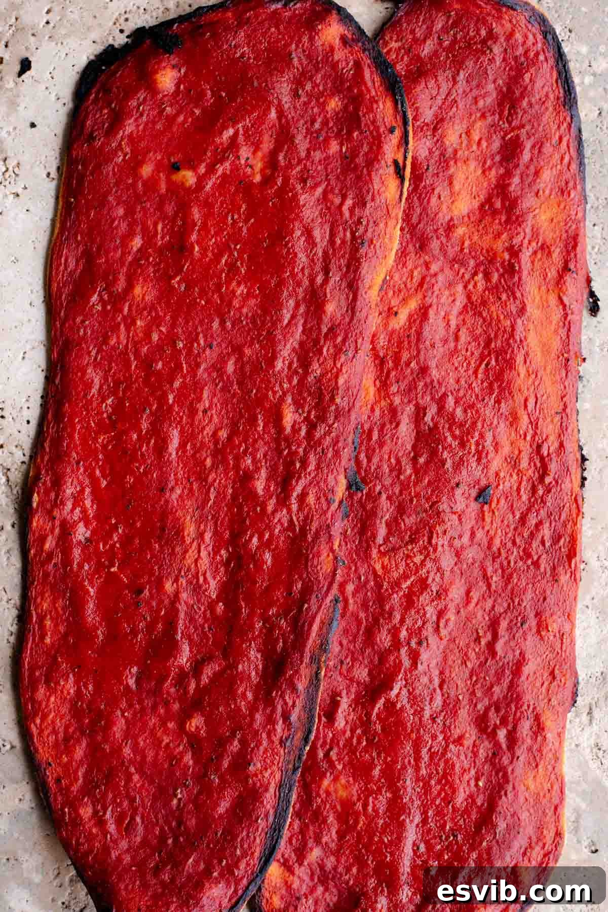 Quick Crispy Pizza Bites 2 Two long thin and crispy pizzas covered in tomato sauce sitting on a travertine surface.