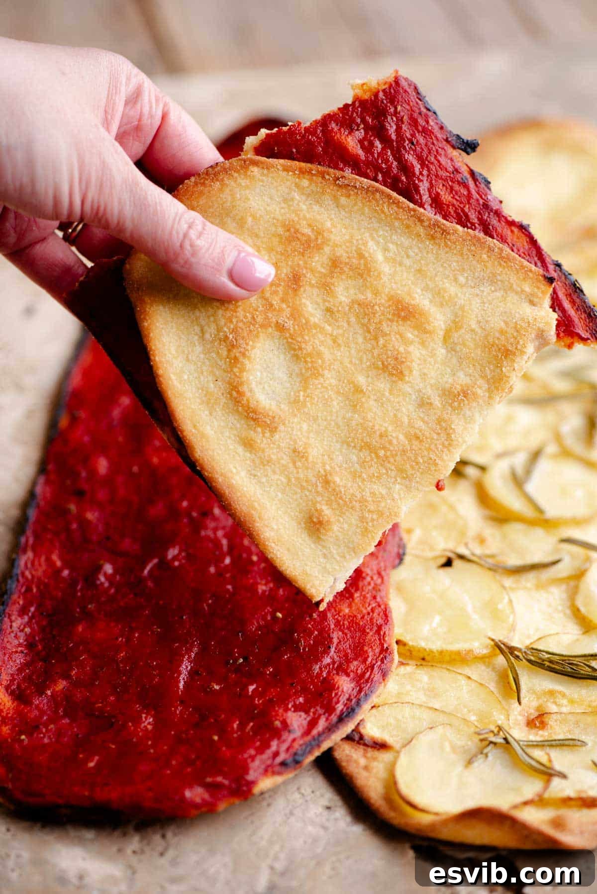 Quick Crispy Pizza Bites 7 A hand holding a thin and crispy pizza folded in half covered in tomato.
