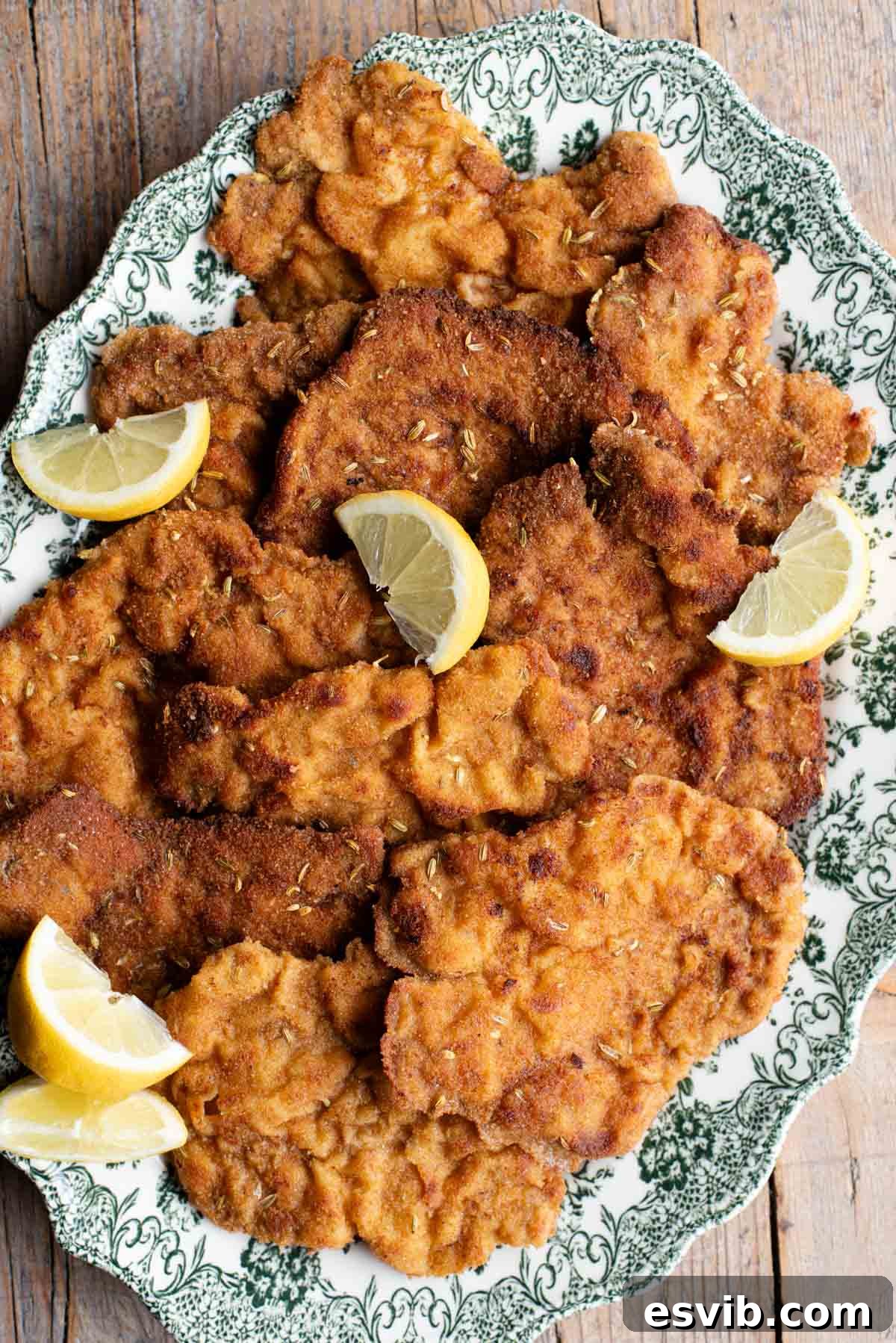 Slices of breaded pork fillet on a serving plate with slices of lemon. The plate is green and white.