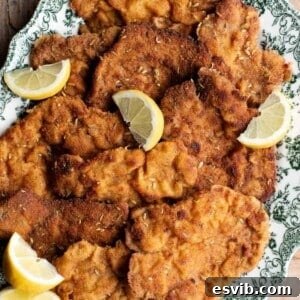 A close up of breaded pork cutlets on a serving plate with lemon wedges.