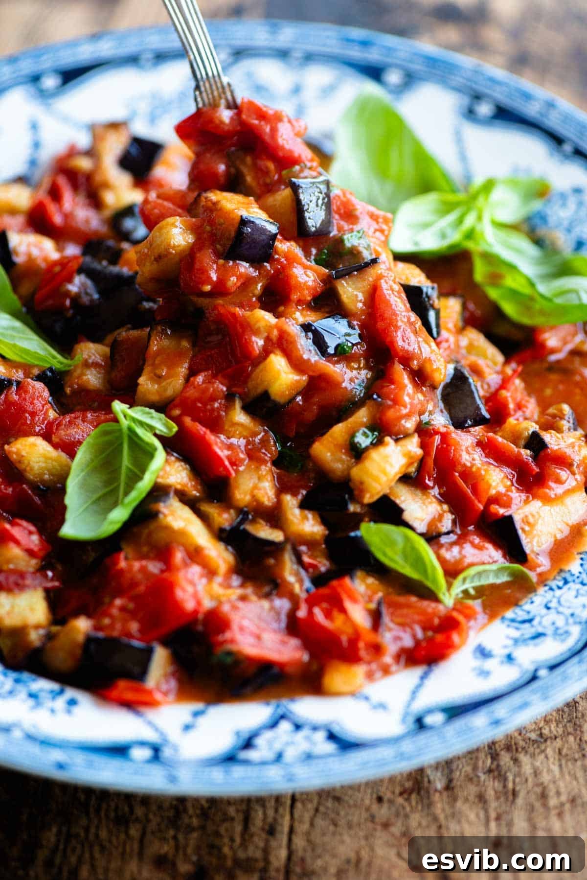 A close up of fried eggplant in tomato sauce in a bowl with fresh basil.