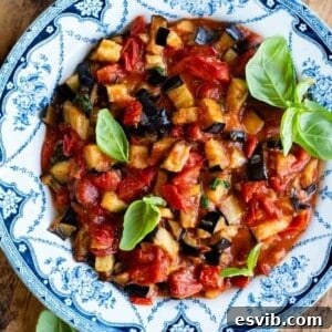 A close up of fried eggplant in a cherry tomato and basil sauce. It's presented in a blue and white country style bowl.
