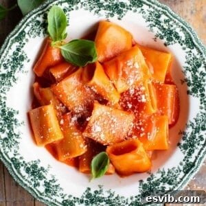 Paccheri pasta in a smooth tomato sauce in a green and white patterned bowl garnished with basil.