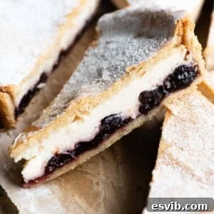 A close up of a slice of ricotta and cherry tart, showing the layers of pastry, jam, and creamy ricotta filling.
