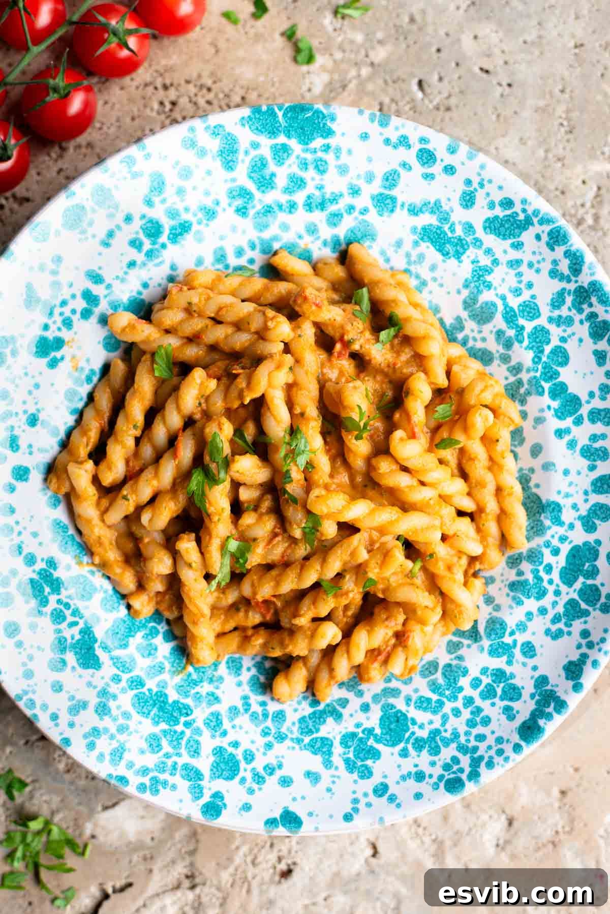 A beautifully plated portion of summer tuna pasta in a blue and white spotted bowl, resting on a rustic travertine surface. The pasta is generously coated in a rich tomato and tuna sauce, garnished with fresh herbs, highlighting its fresh and inviting appearance.
