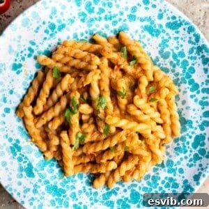 A cropped close-up of tender gemelli pasta coated in a rich and creamy tuna and tomato sauce, presented invitingly in a blue and white speckled bowl.