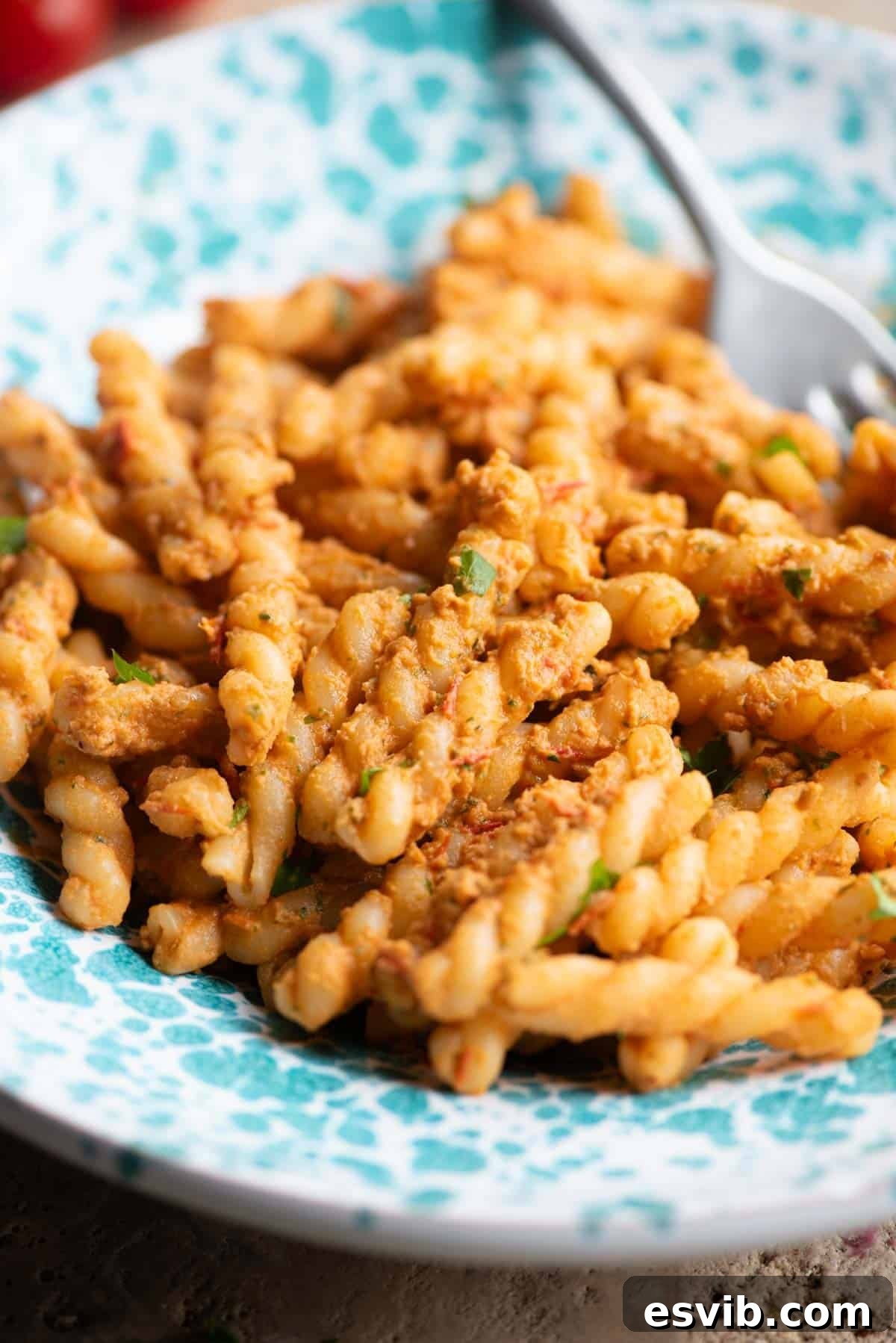 A close-up view of fusilli pasta richly coated in a vibrant tuna and tomato sauce, presented elegantly in a blue and white speckled serving bowl, tempting with its fresh appearance.