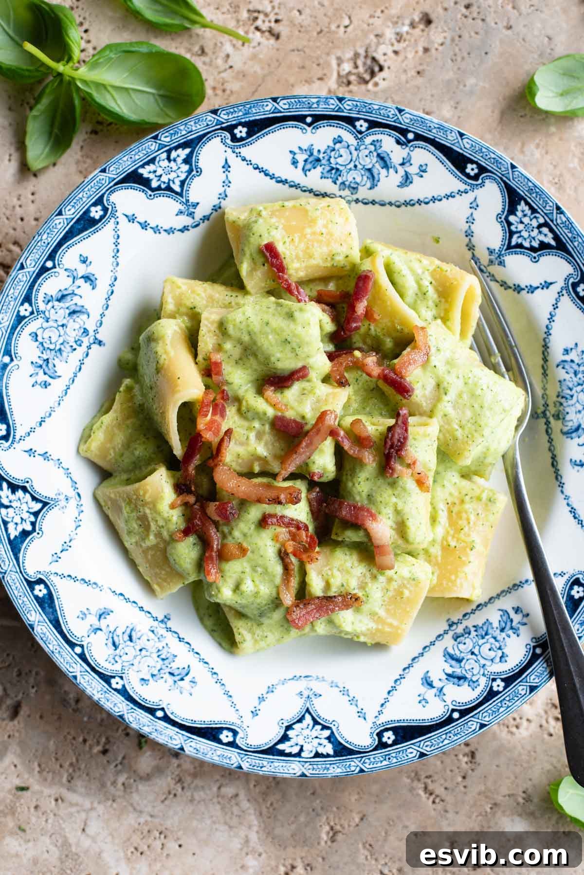 A creamy zucchini pasta in a blue and white bowl topped with crispy pancetta sitting on a travertine surface.