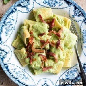 A close up of a creamy zucchini pasta topped with crispy pancetta.
