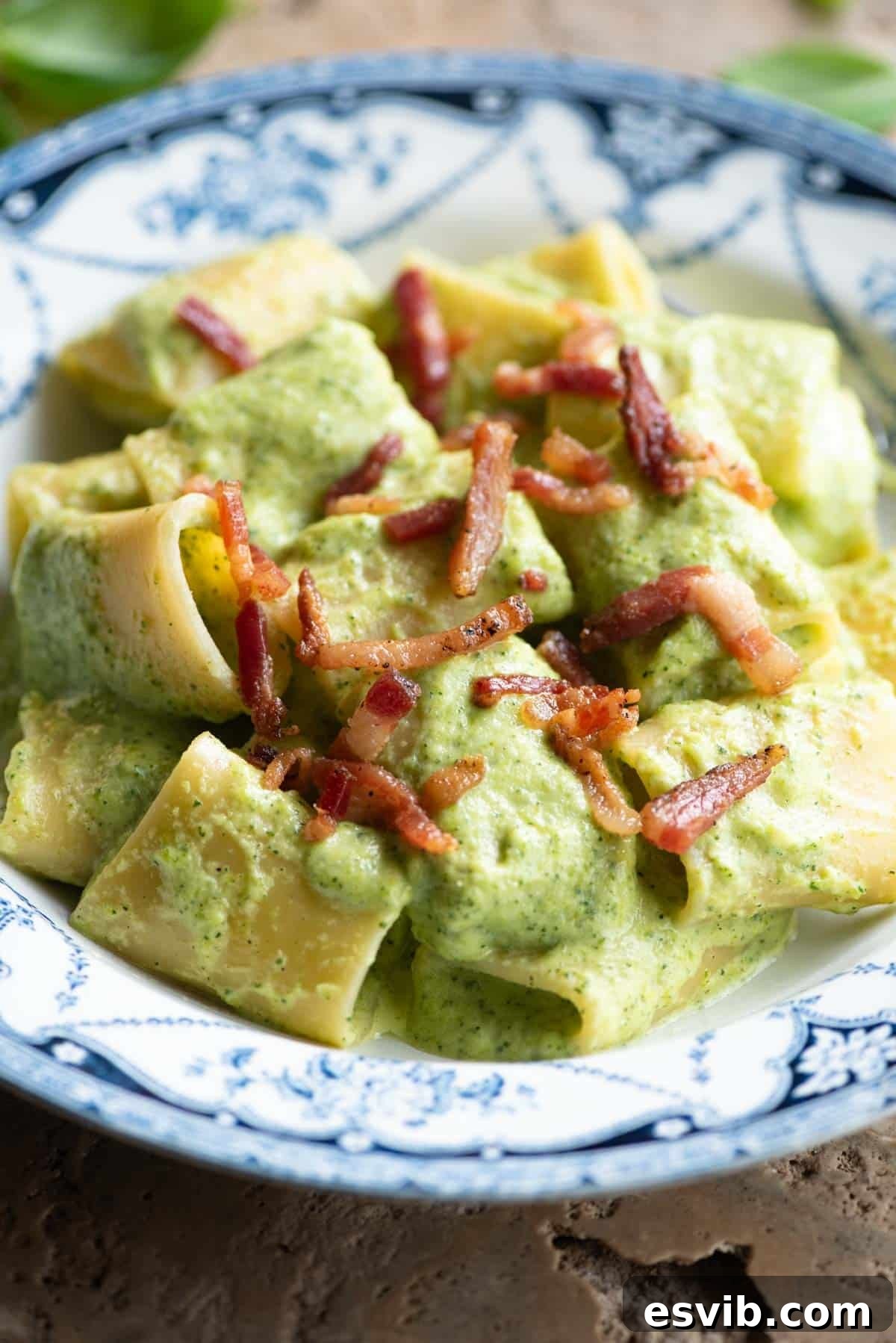 A side shot of paccheri pasta with a creamy zucchini sauce and topped with crispy pancetta. The bowl is blue and white.