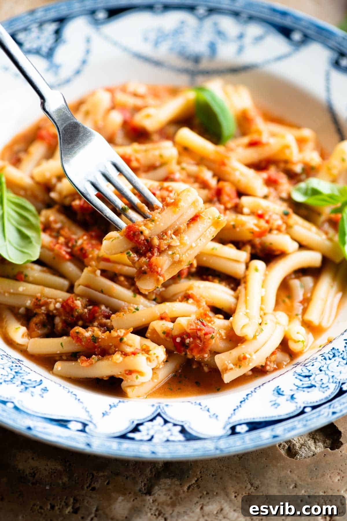 A close up of a fork holing some pasta with a fresh tomato sauce in a blue and white bowl.