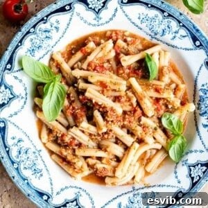 A cropped square image of pasta in tomato sauce in a blue and white vintage style bowl.
