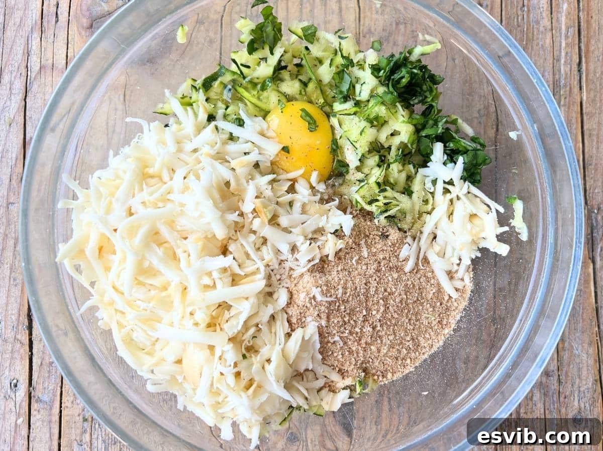 A mixing bowl filled with zucchini, breadcrumbs, cheese, egg, nutmeg, garlic, and basil, ready to be combined.