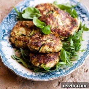 A cropped image showing a stack of perfectly fried zucchini patties with smoked scamorza cheese on a blue and white serving plate, highlighting their golden-brown crust.