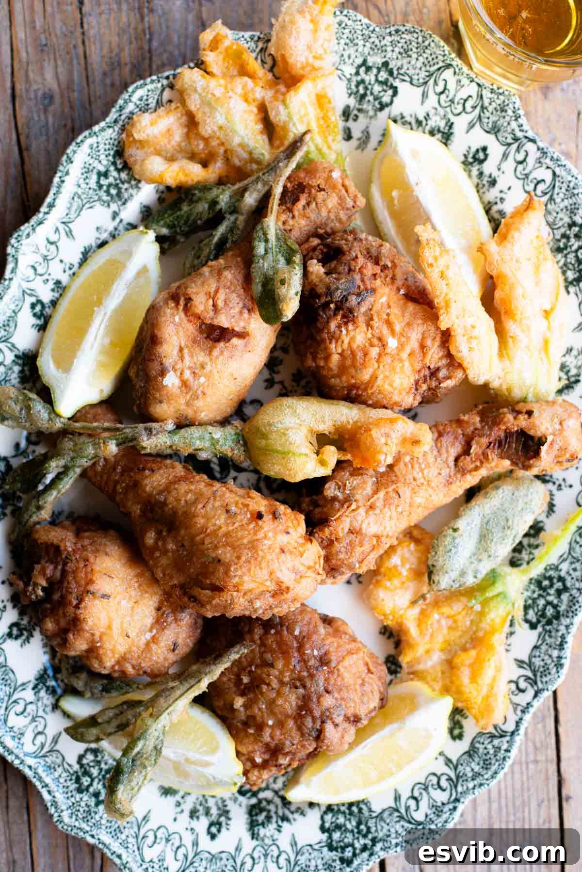 Golden-brown Italian fried chicken arranged on a serving platter, accompanied by delicately fried zucchini blossoms and fragrant sage leaves.