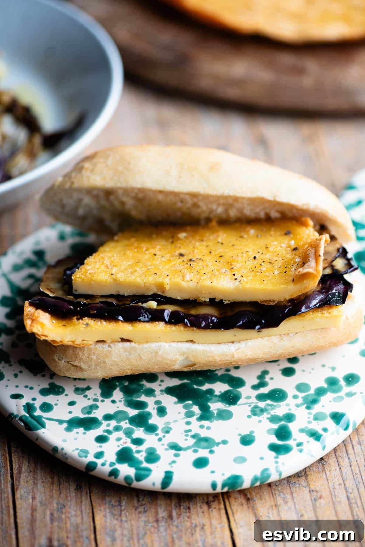 An open view of a 5x5 sandwich, revealing the thick layers of golden chickpea flatbread (farinata) and glistening marinated eggplant slices within a crusty roll.