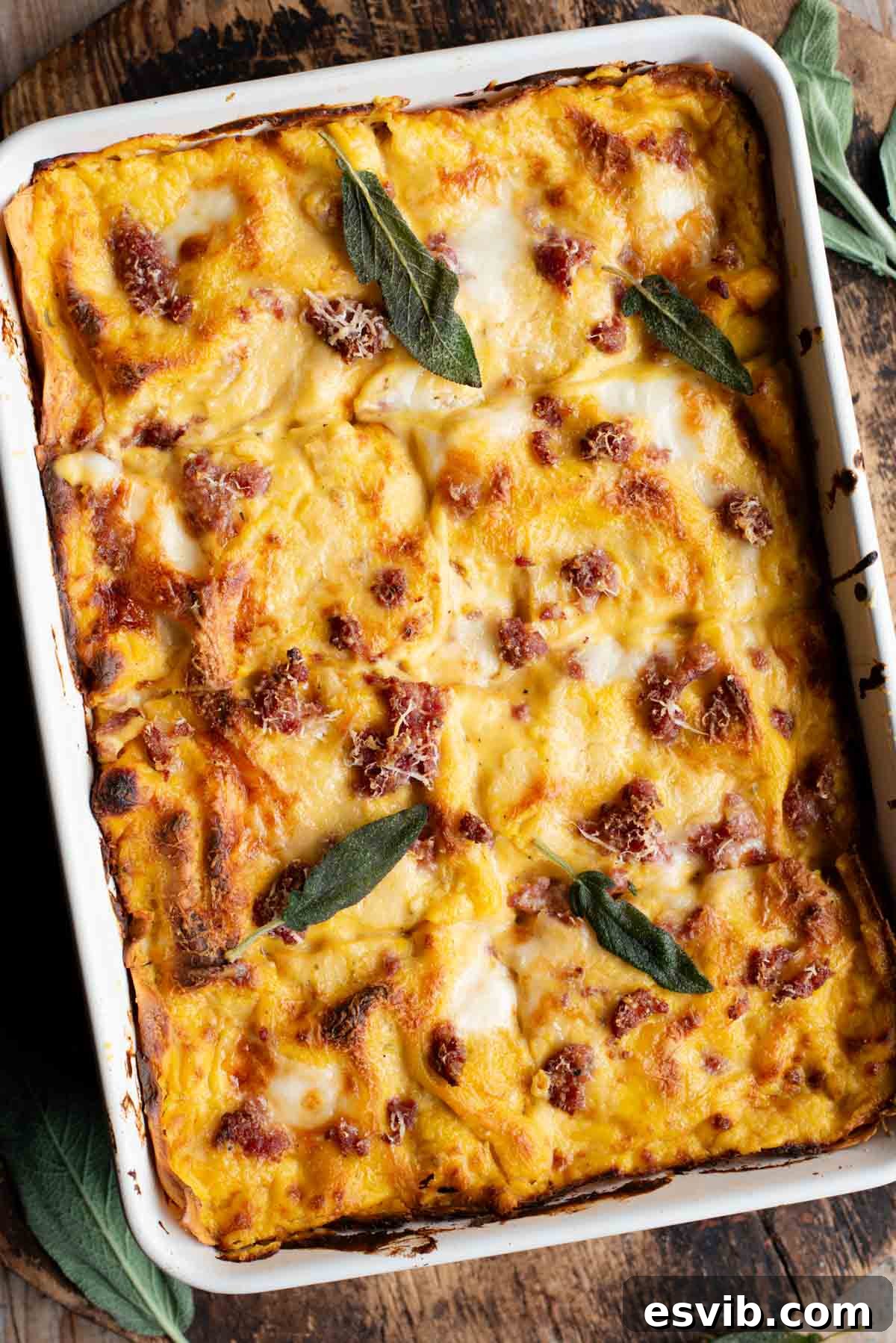 A beautifully baked butternut squash lasagna, generously topped with browned sausage and fresh sage leaves, ready to be served in a rustic baking dish on a wooden surface.