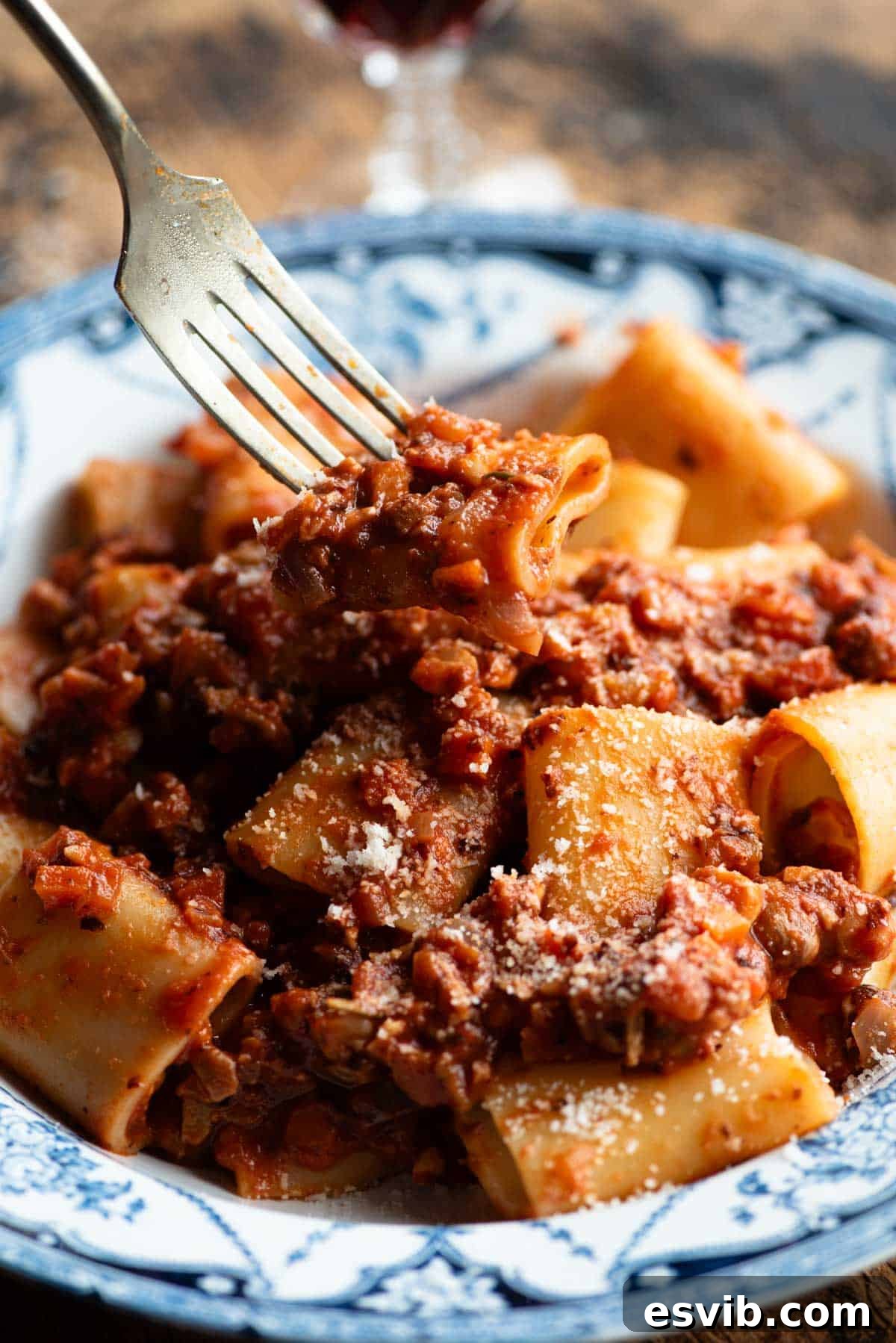Artisan Piedmontese Hazelnut Ragu 6 A close up of a fork holding a piece of paccheri pasta with hazelnut ragu over a rustic blue and white bowl.