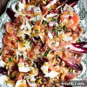 A close up of a festive salad on a serving plate made with blood orange, chicory, fennel, prosciutto, pecorino, pomegranate and pistachios.