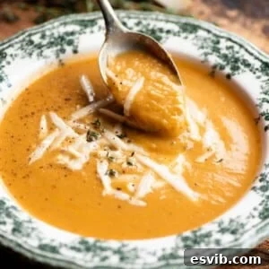 A close up of a spoon picking up some roasted vegetable soup from a green and white vintage style bowl.