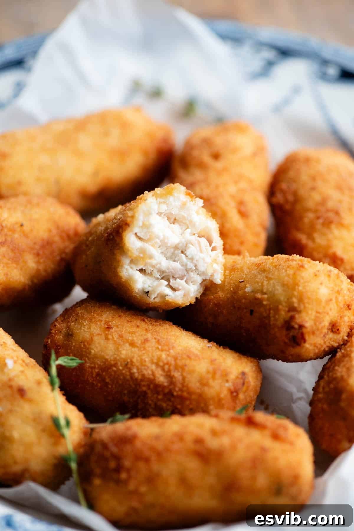 Creamy Chicken Ricotta Bites 6 A tantalizing close-up shot of a half-cut chicken croquette, revealing its creamy ricotta-infused interior, piled on top of other perfectly golden croquettes in a rustic bowl.