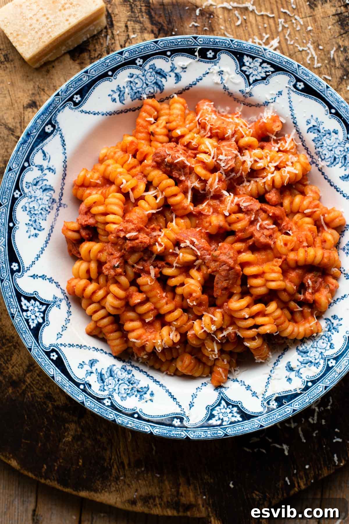 Creamy tomato pasta with sausage in a blue patterned bowl on a wooden serving board.