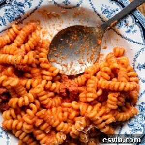 A close up cropped image of creamy tomato sausage pasta in a blue bowl with a serving spoon