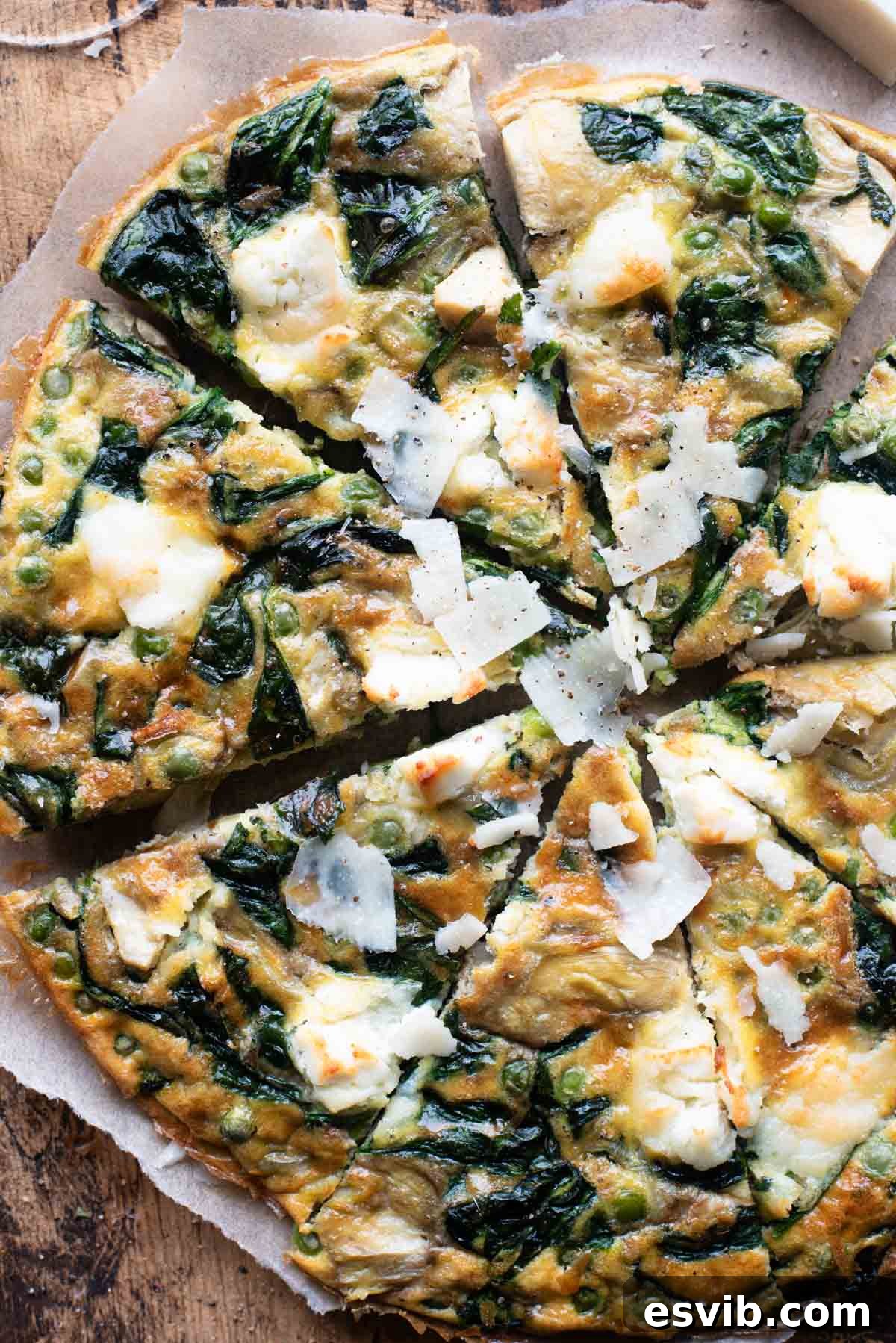 An overhead shot of a spinach and artichoke frittata cut into slices sitting on a wooden cutting board, garnished with fresh herbs.