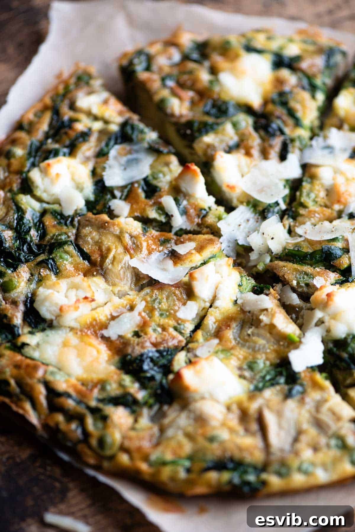 A close up of a spinach and artichoke frittata topped with goat's cheese cut into slices, showing its creamy texture.